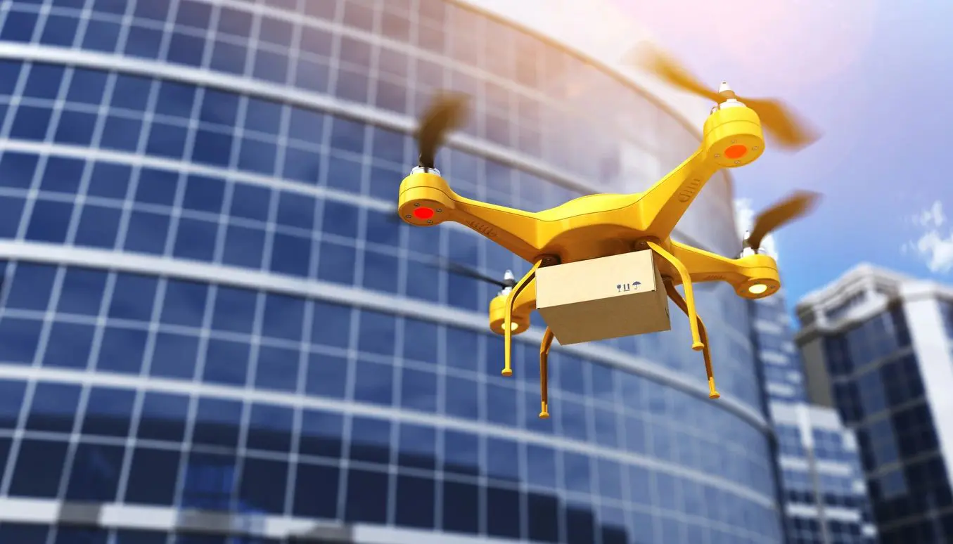 A yellow drone flying in front of a building.